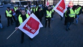 Mitarbeiter eines privaten Busunternehmens stehen mit Fahnen der Dienstleistungsgewerkschaft Verdi bei einem Warnstreik vor dem Unternehmen. (Foto: dpa Bildfunk, picture alliance/dpa | Bernd Weißbrod) Mitarbeiter eines privaten Busunternehmens stehen mit Fahnen der Dienstleistungsgewerkschaft Verdi bei einem Warnstreik vor dem Unternehmen.