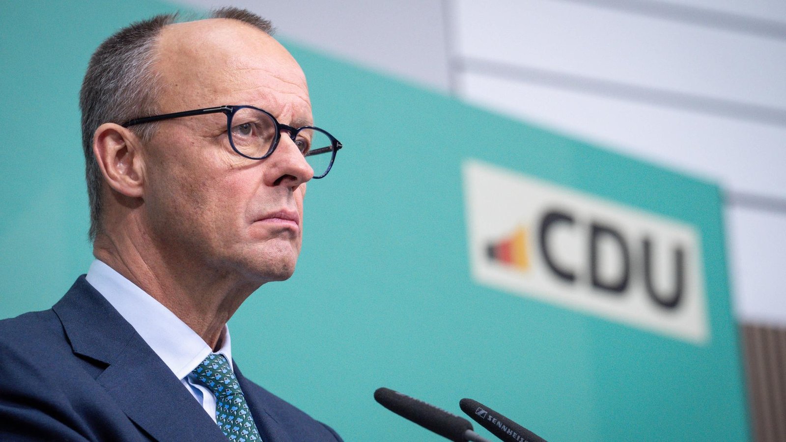 Merz steht bei einer Pressekonferenz mit ernstem Blick am Mikrofon vor einem türkisen Hintergrund mit dem Logo der CDU. Merz steht bei einer Pressekonferenz mit ernstem Blick am Mikrofon vor einem türkisen Hintergrund mit dem Logo der CDU.